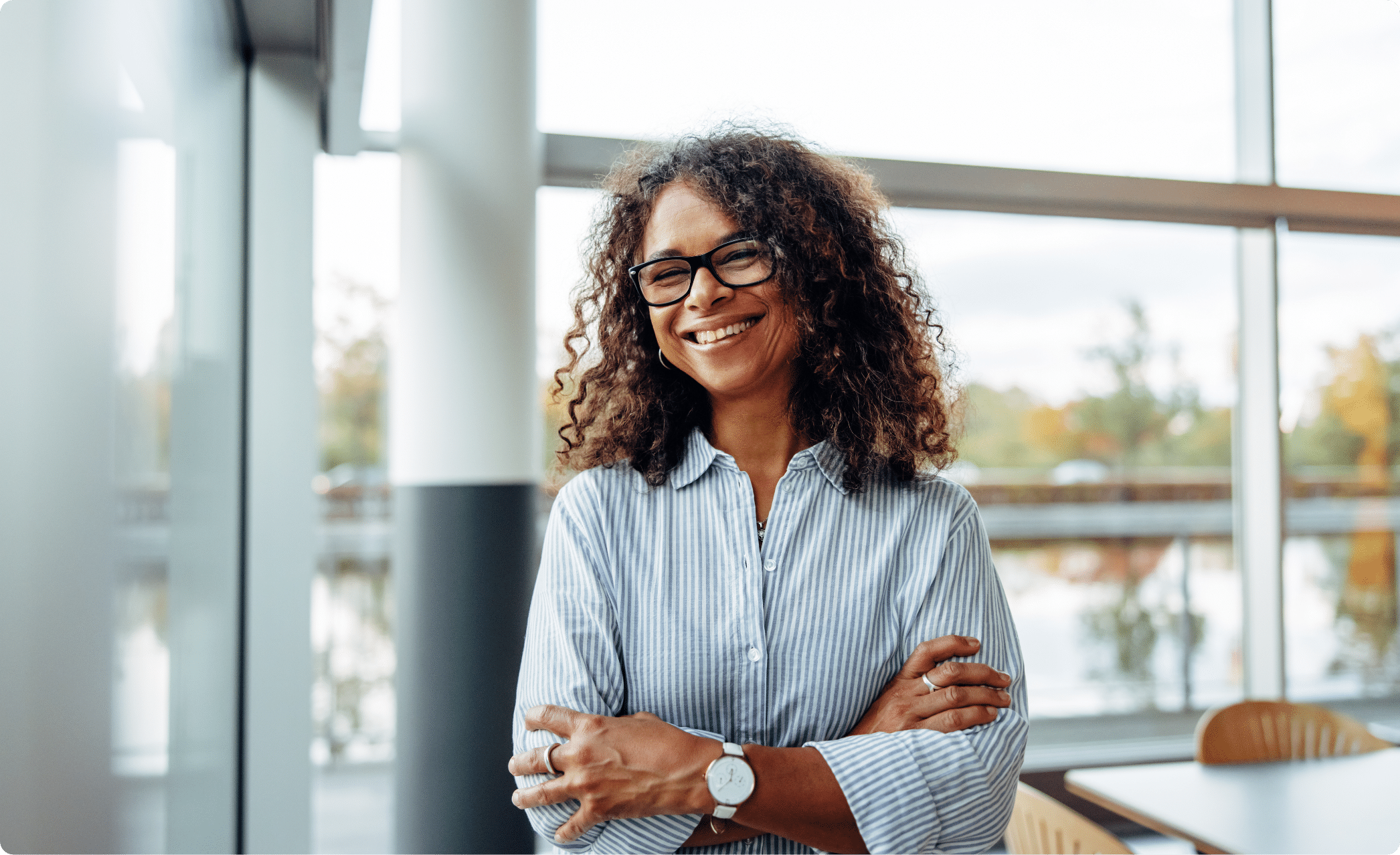 A woman in a business office with lots of windows standing with her arms crossed and smiling
